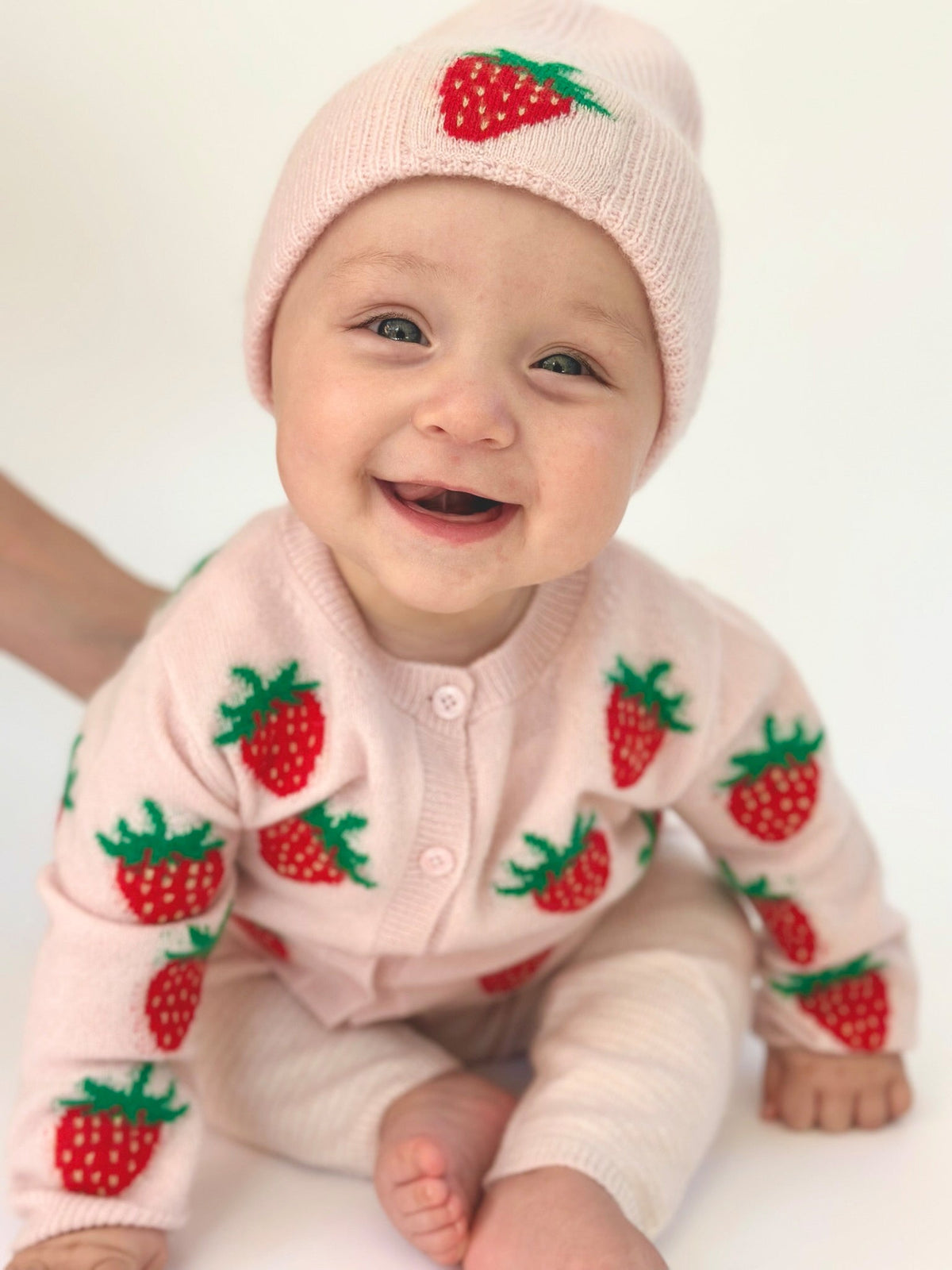 lachendes baby sitzend im erdbeer outfit